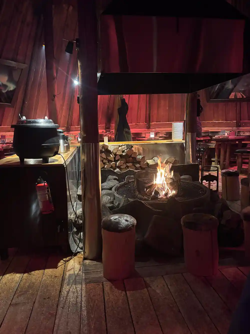 Inside the Gamme: a fire pit, a cooking pot and benches under a timber roof
