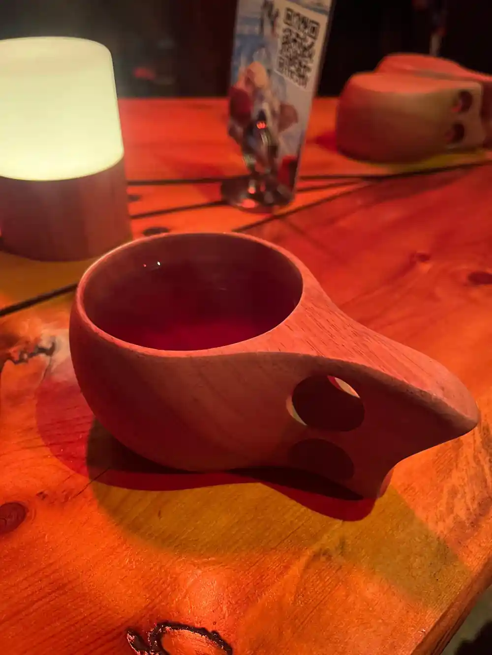 A traditional carved wooden kuksa cup on a table lit by firelight