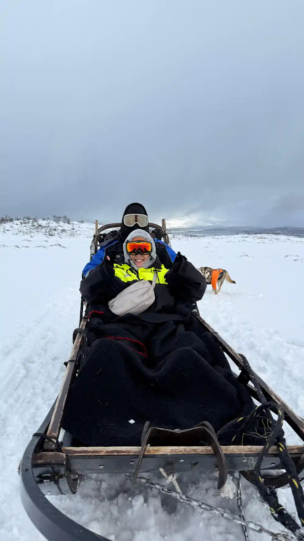 Two passengers in goggles and thermal suits riding in the sled basket