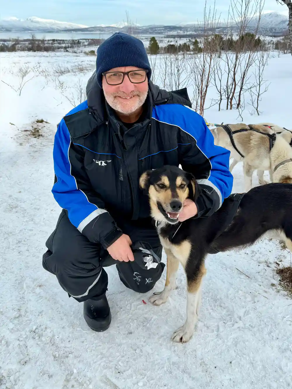 A visitor kneeling with an arm around a sled dog beside the team